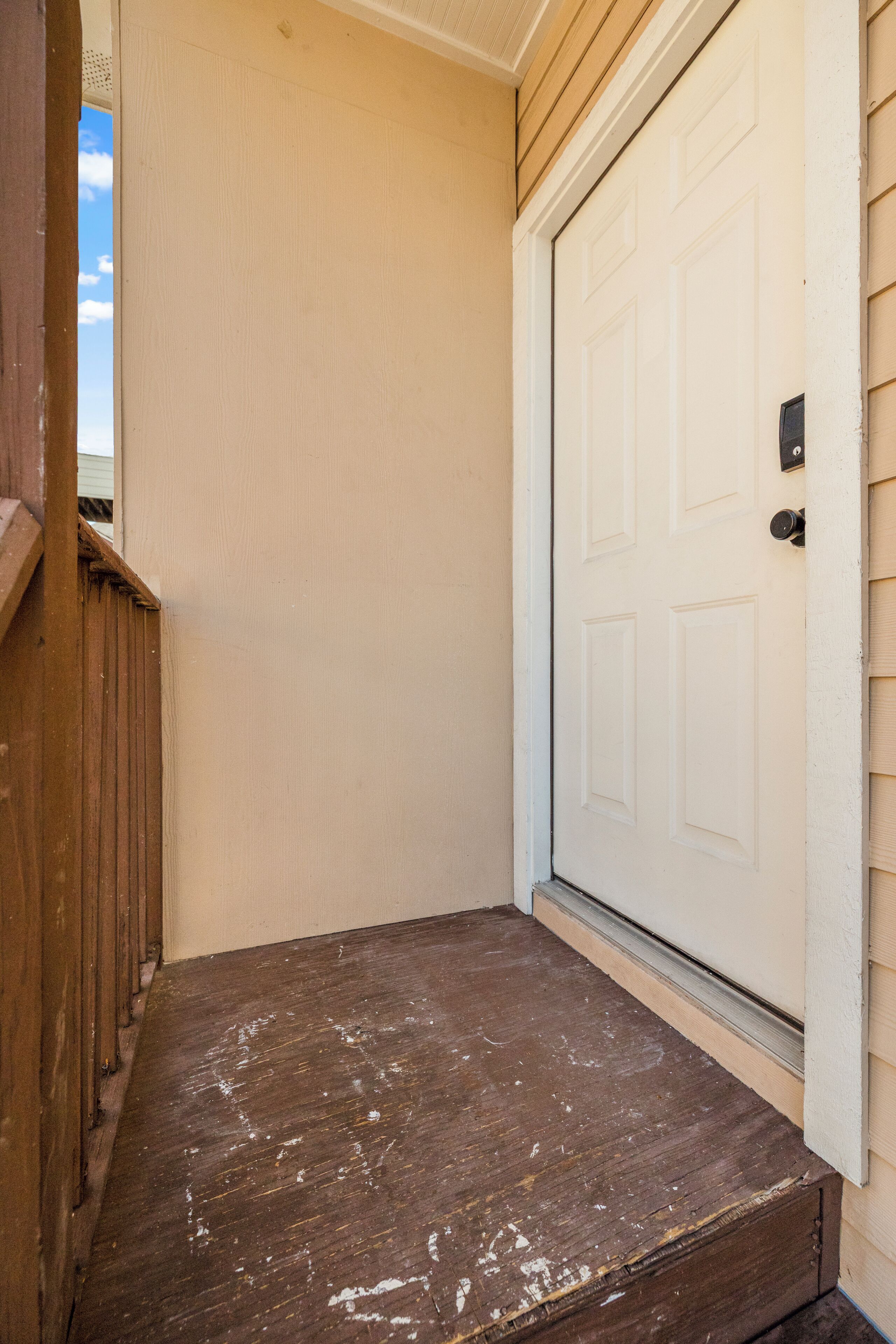 Une terrasse en bois mène à une porte blanche, avec une boîte aux lettres sur le côté droit.