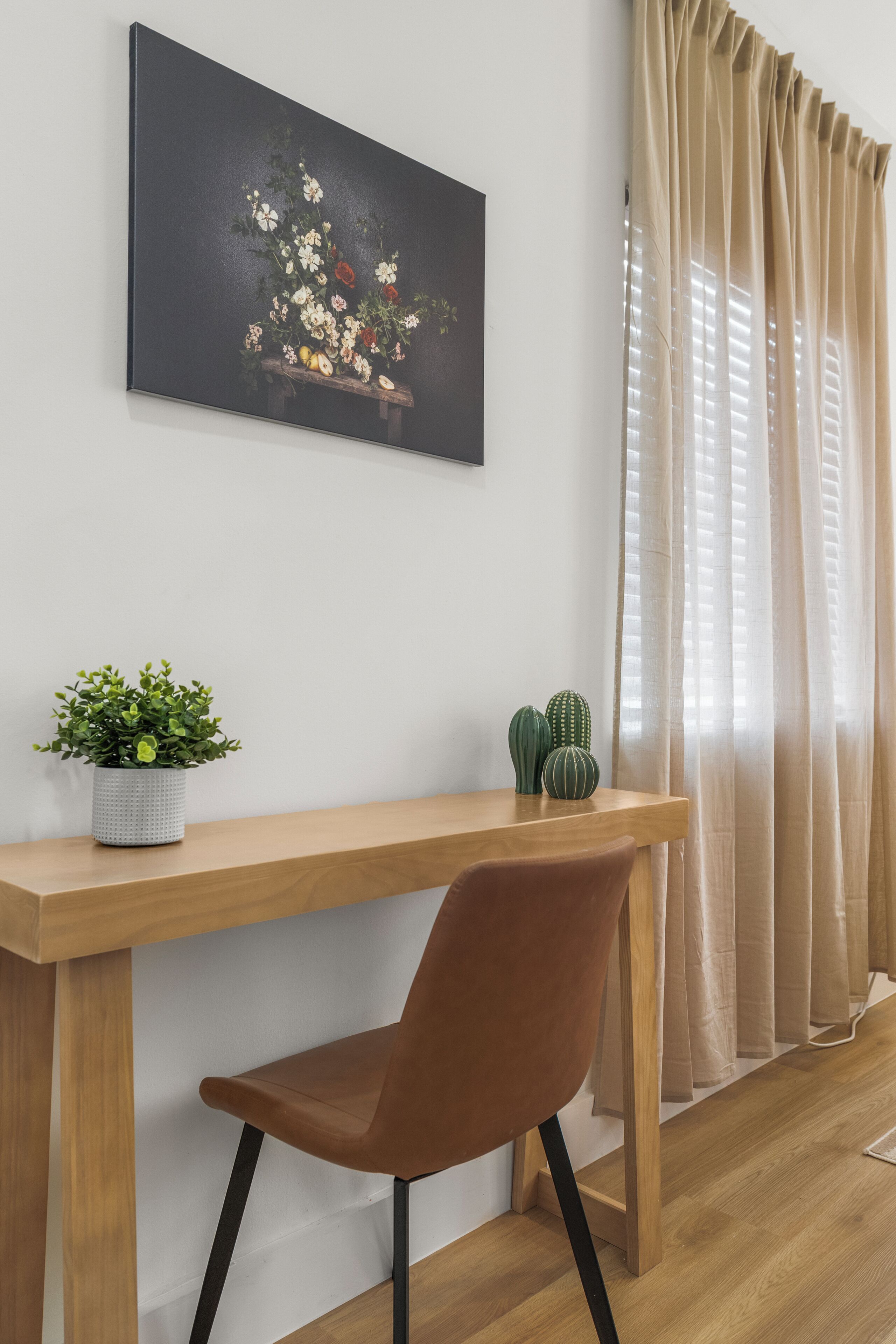 Une pièce avec un bureau en bois, une chaise marron, une plante en pot et un cactus posé sur le bureau.