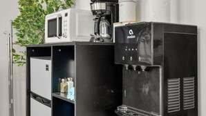 Angolo cottura con forno a microonde, macchina del caffè, dispenser di acqua e TV a parete.