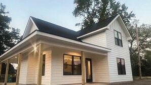 A two-story house with a covered porch, large windows, and a dark roof. - "Pike's Place" New Cabin in Daisy Ark. (Kirby)