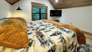 A bedroom with a large bed, a ceiling fan, a window, and a TV. - "Pike's Place" New Cabin in Daisy Ark. (Kirby)