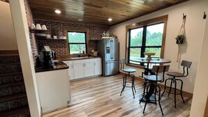 A kitchen with a brick wall, wooden flooring, a refrigerator, and a dining area with a table and chairs. - "Pike's Place" New Cabin in Daisy Ark. (Kirby)