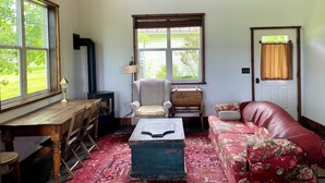 A cozy living room with a wooden ceiling, a red patterned rug, a floral sofa, a wooden coffee table, a lamp, a chair, and a window with a view of greenery. - Bozeman Farmhouse Cottage (Bozeman)