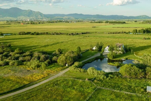 A rural landscape with a house surrounded by fields, a small pond, and distant mountains. - Bozeman Farmhouse Cottage (Bozeman)
