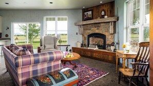 Ein Wohnzimmer mit einem karierten Sofa, einem Holzstuhl, einem Kamin und Blick ins Freie.