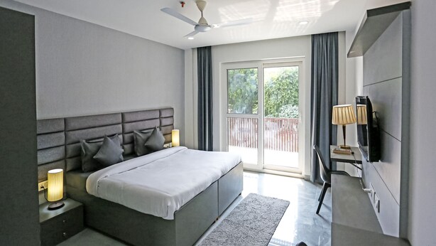 Un dormitorio moderno con cama, lámparas de noche, ventilador de techo, televisor y puerta corrediza de vidrio al exterior.