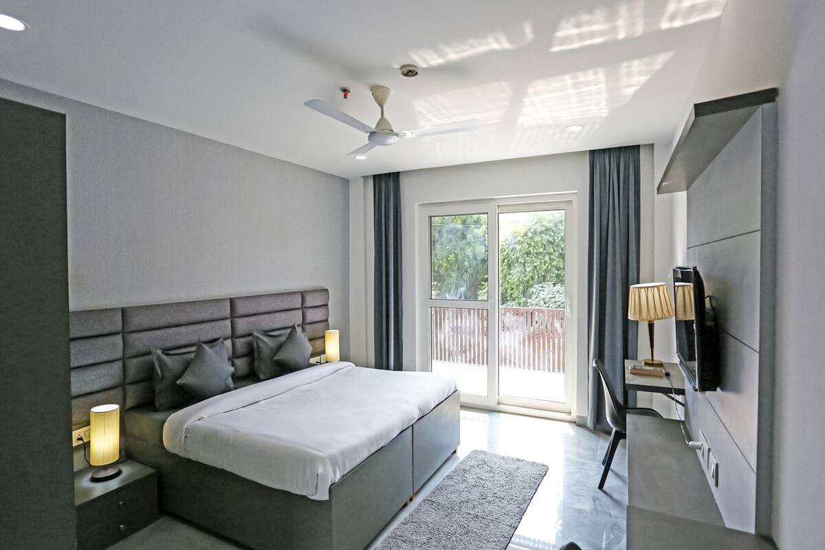 Ein modernes Schlafzimmer mit Bett, Nachttischlampen, Deckenventilator, Fernseher und einer Schiebeglastür nach draußen.