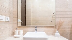Un baño con un espejo grande, un lavabo blanco y un florero con plantas secas.