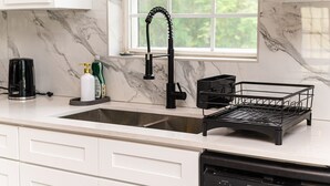 A kitchen with a black faucet, a coffee maker, and a dish rack on the counter.