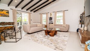 A spacious living area with a glass coffee table, a beige sofa, and a dining table with chairs.