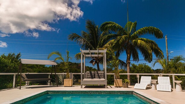 A pool area with lounge chairs, a pergola, and palm trees.