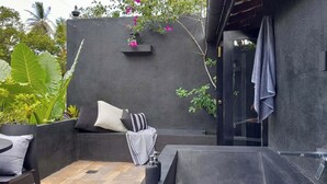 Un espacio de estar al aire libre moderno con una pared negra, un pequeño estante con flores y una toalla colgada en la pared.
