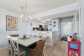 A dining area with a table and chairs, a kitchen with white cabinets, and a hallway leading to a door.