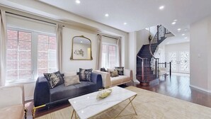 A spacious living room with a dark sofa, a white coffee table, and a staircase leading to an upper floor.
