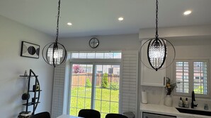 A modern kitchen with a marble island, pendant lights, and a view of the backyard.
