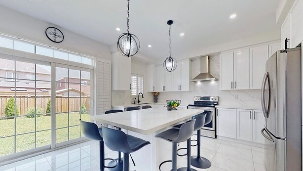 A modern kitchen with white cabinets, a large island with bar stools, stainless steel appliances, and pendant lighting.