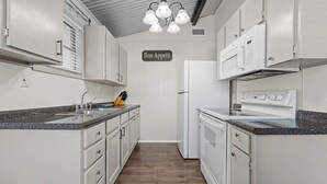 A kitchen with white cabinets, a granite countertop, a stove, and a refrigerator.
