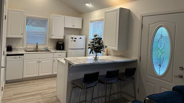 A compact kitchen with white cabinets, a built-in refrigerator, a coffee maker, and a small island with bar stools.