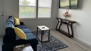 A living room with a dark blue sofa, a small white table, and a dark wooden console table with a vase of flowers.