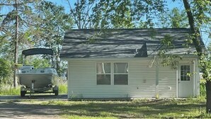 A small, single-story house with a front door and a window, situated next to a trailer with a boat on a trailer.