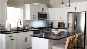A modern kitchen with white cabinets, stainless steel appliances, and a central island with bar stools. - The Little Boise Bungalow (Boise)