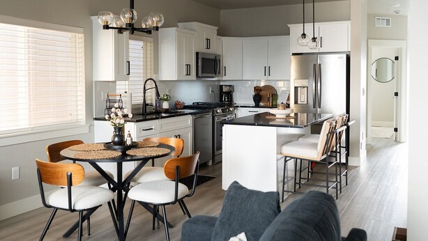 A modern kitchen with white cabinets, a stainless steel refrigerator, and a dining area with a round table and chairs. - The Little Boise Bungalow (Boise)
