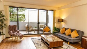 Una sala de estar moderna con sofá, sillón, mesa de centro y un puerta corrediza de vidrio que da a un área exterior con una mesa y sillas.