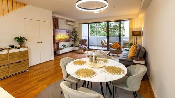 Una sala moderna con una mesa de comedor redonda, sillas tapizadas en gris, un sofá y un amplio ventanal con vistas al exterior.