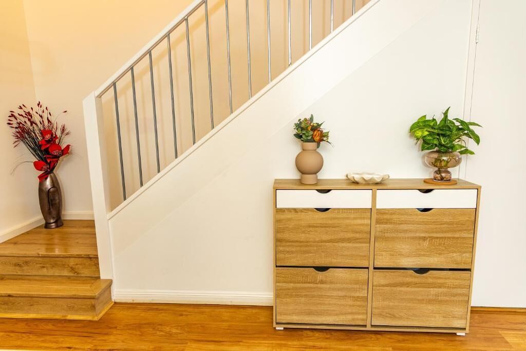 Un escalier avec des finitions en bois, un mur de couleur beige et un meuble en bois doté de deux tiroirs et d’une étagère.