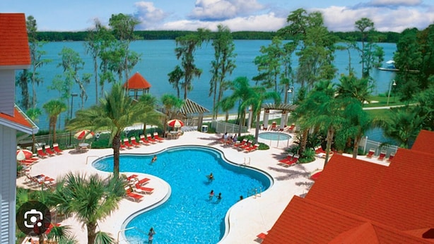 Ein Resort mit einem großen Schwimmbad, umgeben von Palmen, Liegestühlen, einem Pavillon und Blick auf das Wasser.