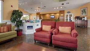 Eine Hotellobby mit einer Rezeption, einem grünen Sofa, zwei roten Sesseln und einer großen Pflanze in einem Topf.
