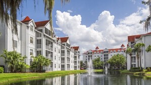 Ein Hotel direkt am Wasser, bestehend aus mehreren Gebäuden, mit einer zentralen Fontäne und üppiger Bepflanzung.