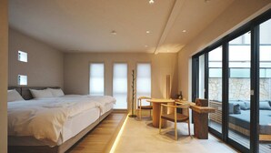 Ein modernes Schlafzimmer mit einem großen Bett, einem kleinen Tisch und einer Sitzecke mit Blick ins Freie.