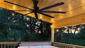 Un bain à remous sur une terrasse en bois, agrémentée d’un ventilateur de plafond et de guirlandes lumineuses.