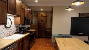 Keittiössä on puiset kaapit, mikroaaltouuni, pesuallas sekä ruokailutila, jossa on pöytä ja tuolit.