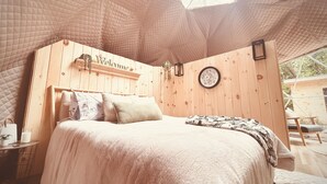 A cozy bedroom with a wooden headboard, a welcome sign, a bedside table with a candle, and a view of the outdoors through a skylight. - • TRANQUILITY DOME• OFFGRID GLAMPING RETREAT IN PRIVATE FOREST! (Killaloe)