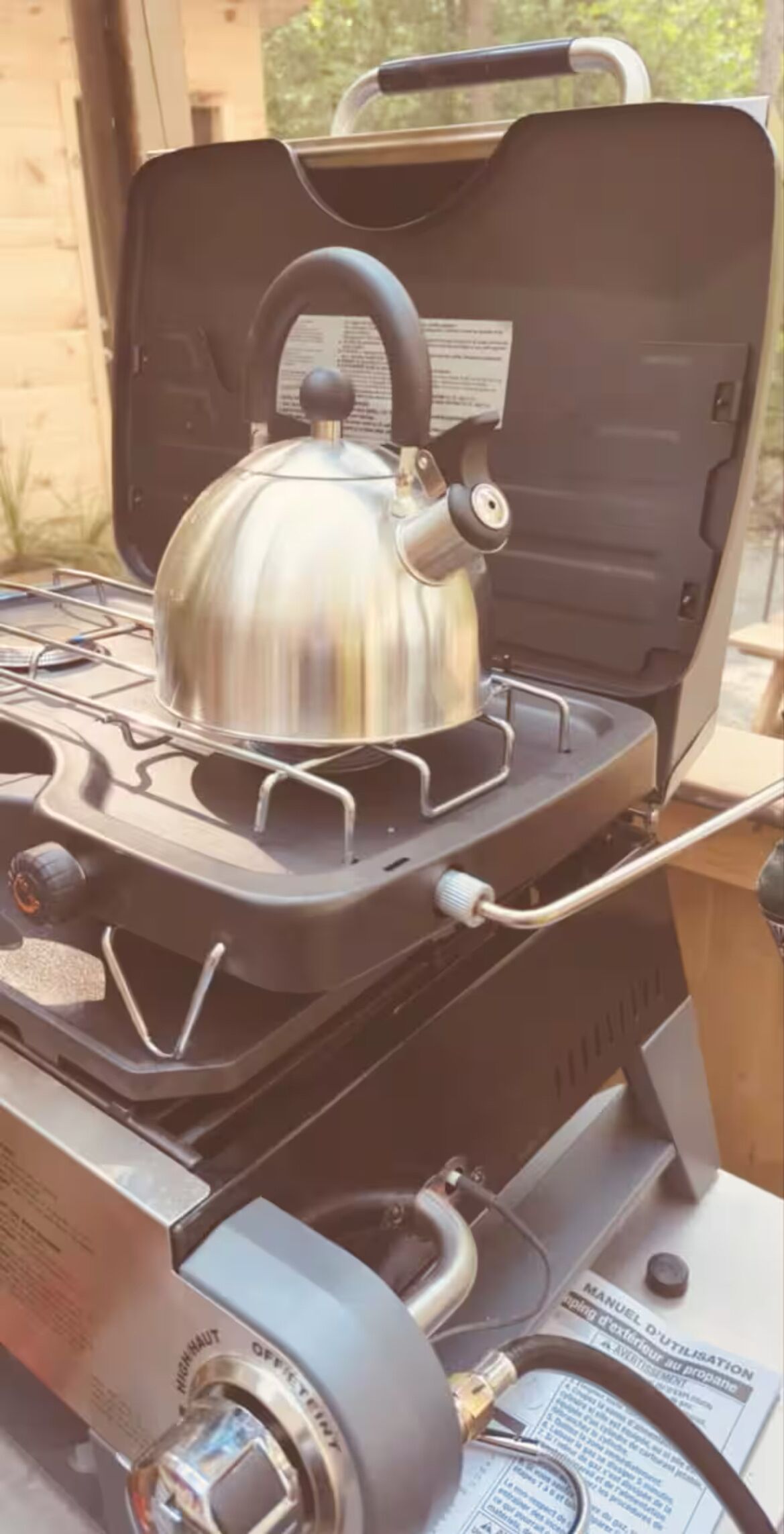 Une cuisinière à gaz portable, avec une bouilloire posée sur le dessus, un panneau de commande et un tuyau à gaz.