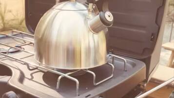 Une cuisinière à gaz portable, avec une bouilloire posée sur le dessus, un panneau de commande et un tuyau à gaz.