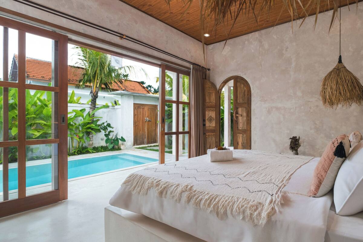 A bedroom with a large bed, a view of a swimming pool, and a rustic ceiling.