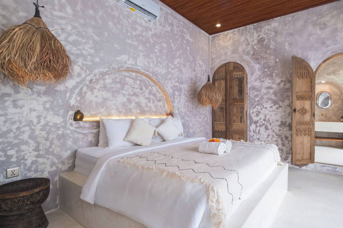 A bedroom with a large bed, a hanging light fixture, and a wooden door with a mirror.
