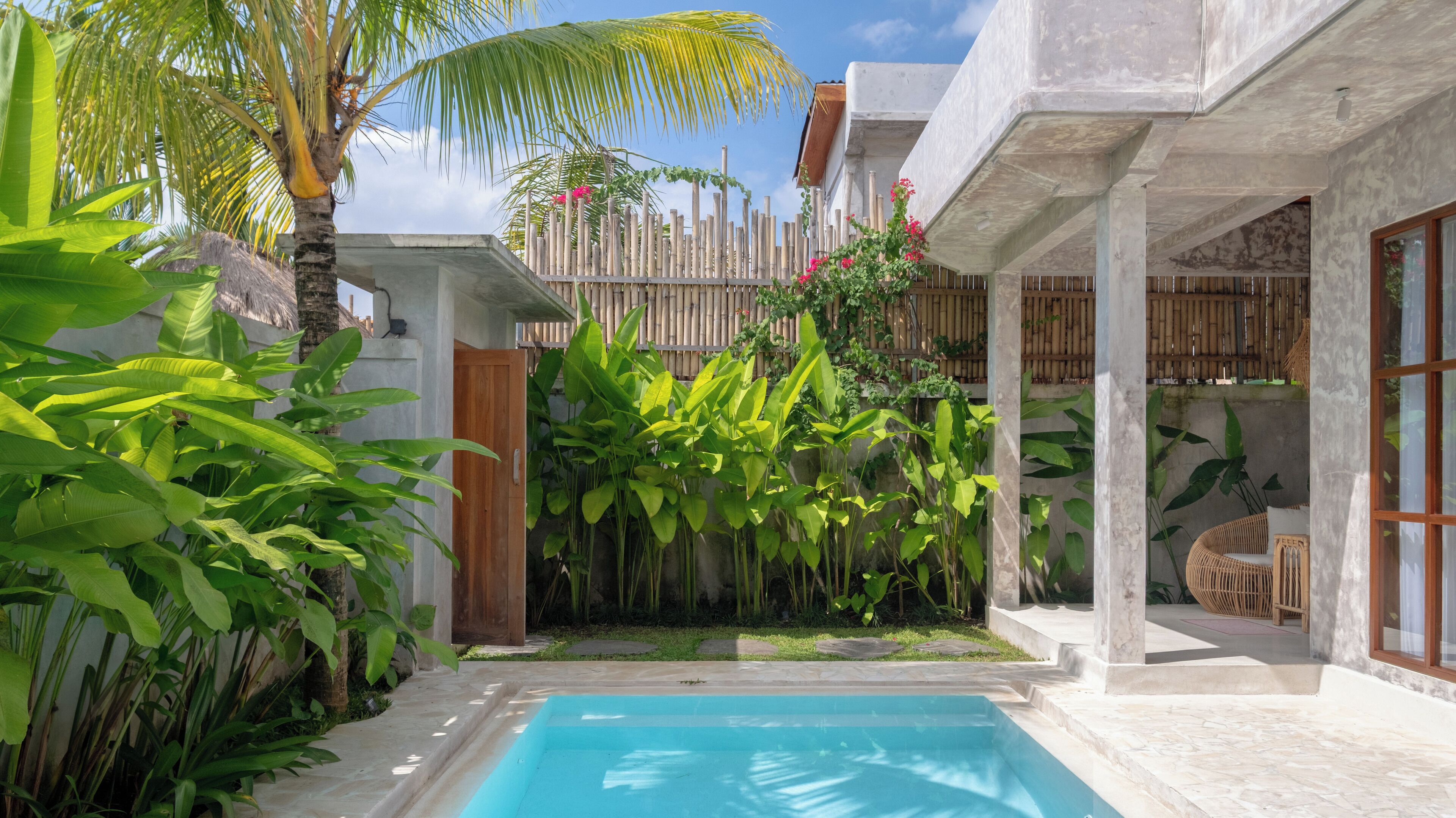 Zona de piscina con plataforma de hormigón, rodeada de exuberante vegetación tropical y una valla de bambú.