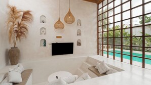 A modern living room with a flat-screen TV, a large window with a view of a pool, and a decorative wall with small niches. - Nick Villas by Villa Finder (Ubud)