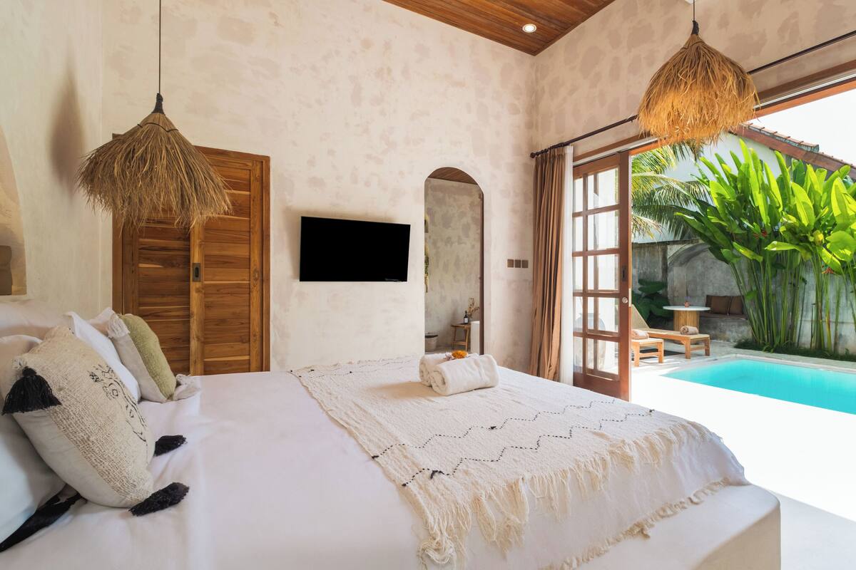 A bedroom with a large bed, a TV, and a view of a swimming pool.