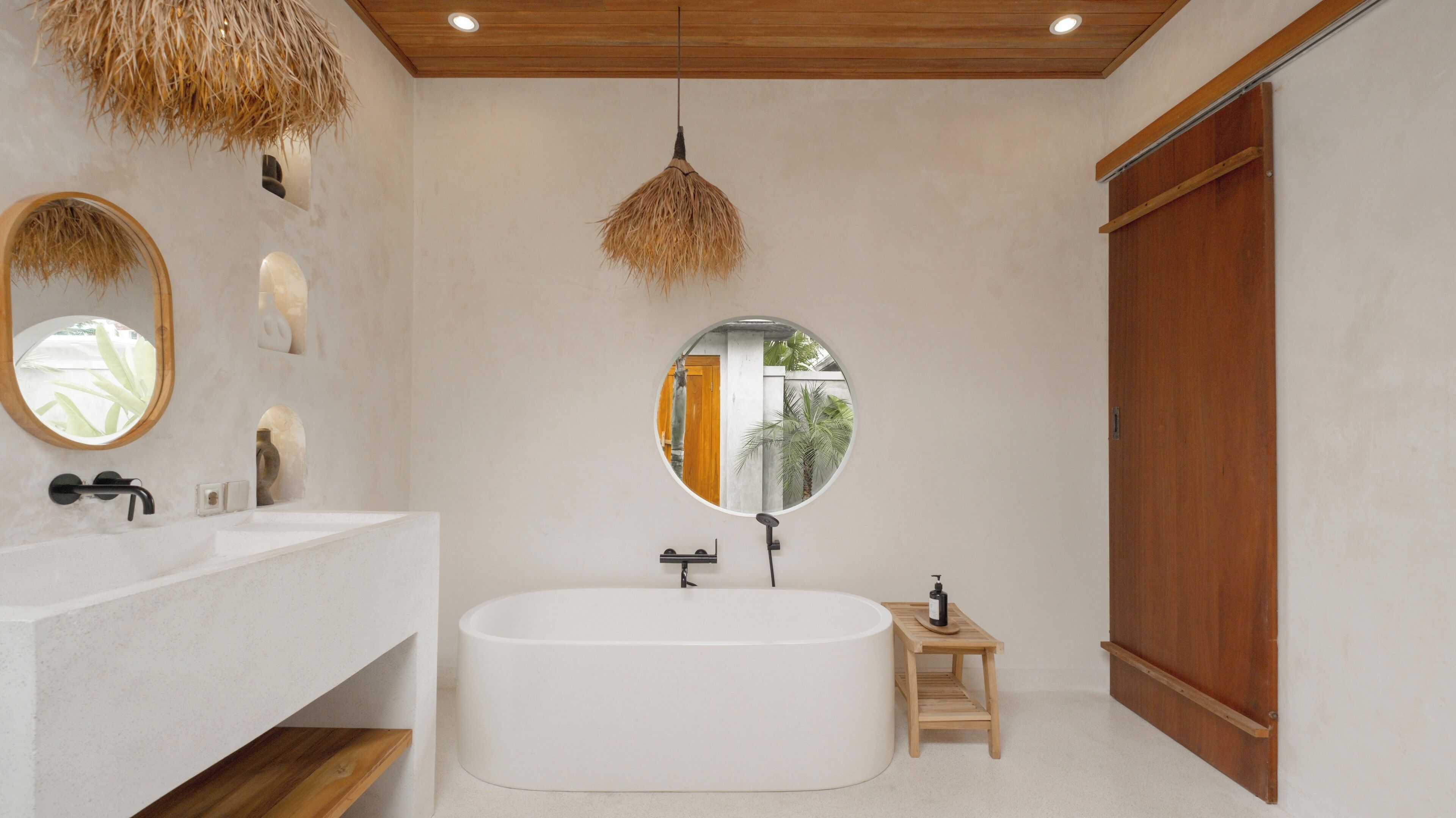 Een moderne badkamer met een vrijstaand bad, een ronde spiegel en een houten deur.
