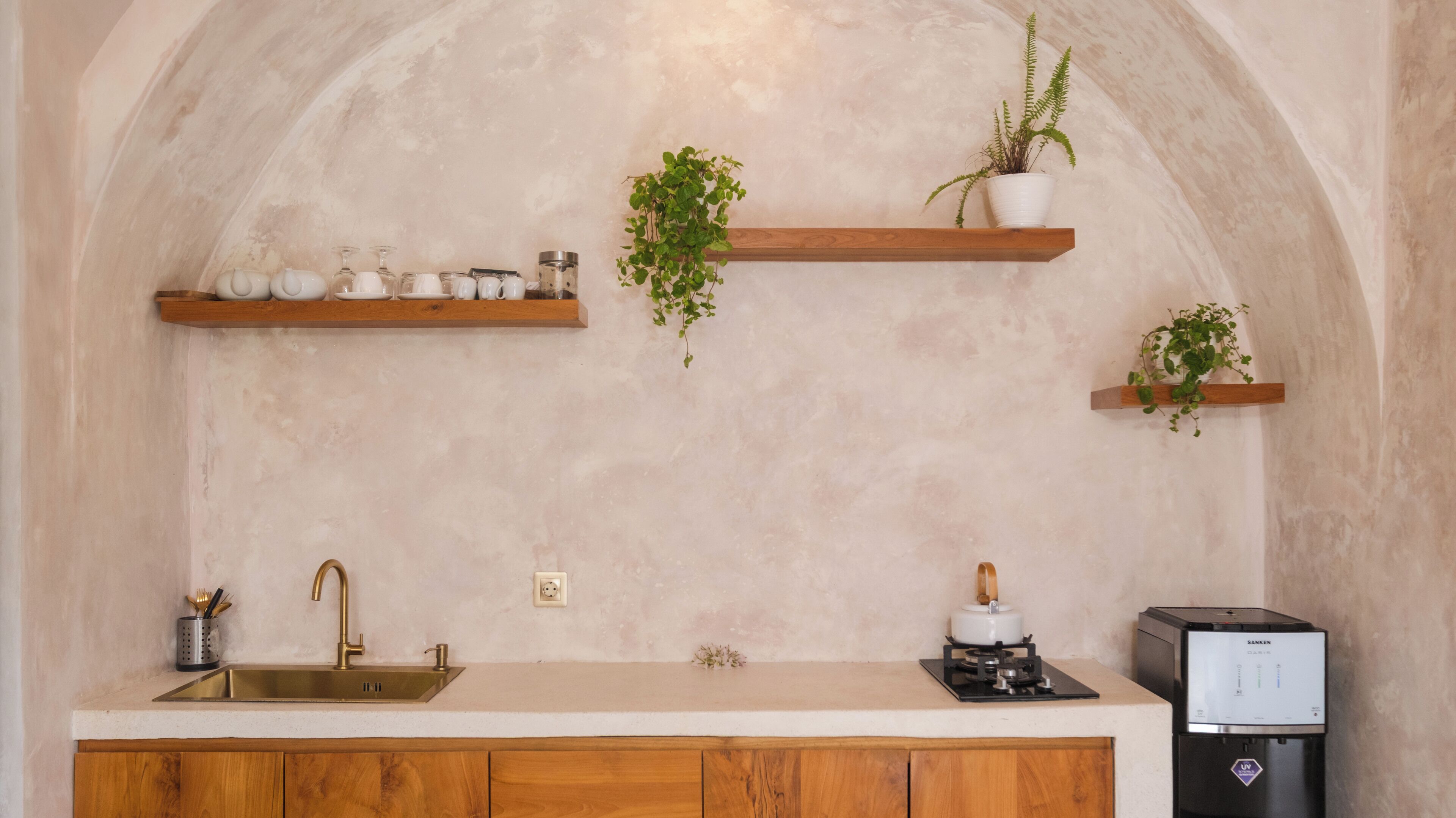 Una cocina con encimera de madera, un lavamanos de acero inoxidable, un horno empotrado y dos estantes de madera con plantas en macetas.