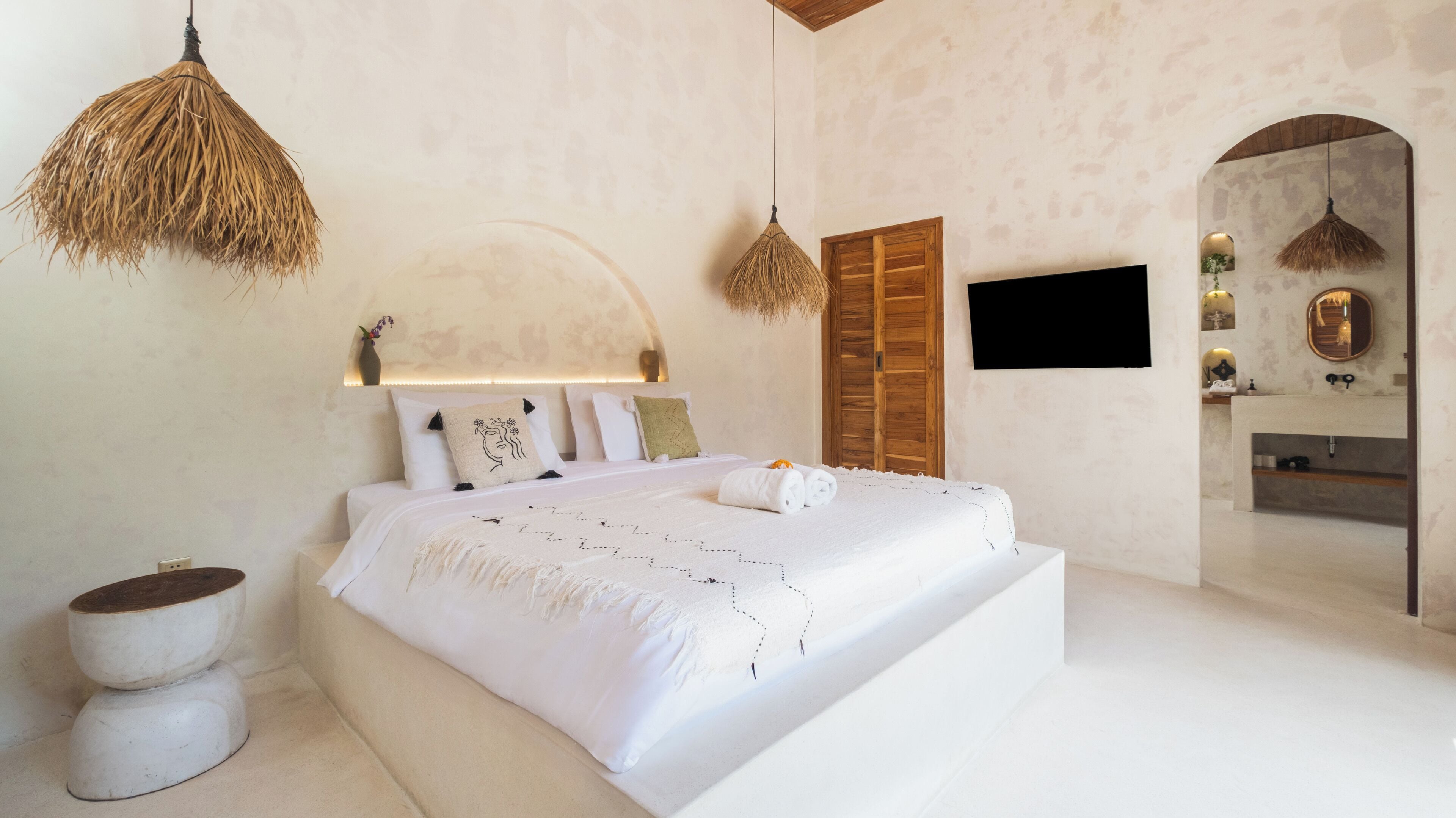Une chambre moderne avec un grand lit, une armoire en bois, une télévision et une salle de bain visible à travers une arche.