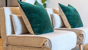 Ein Sofa mit grünen und weißen Kissen, Holzbeinen und hellem Stoff.