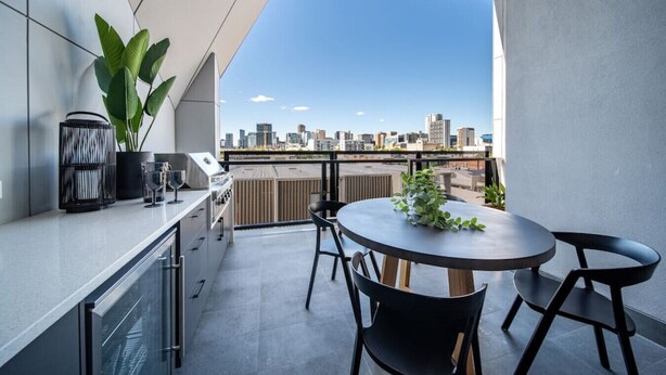 A modern kitchen with a city view, a round table with chairs, and a potted plant.