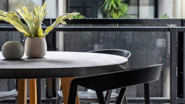 Un área de estar moderna al aire libre con una mesa redonda y sillas negras, que incluye una planta en maceta y un objeto esférico sobre la mesa.