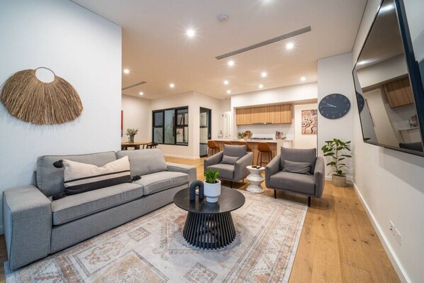 Ein modernes Wohnzimmer mit einem grauen Sofa, zwei Sesseln, einem Couchtisch und einer Küche im Hintergrund.
